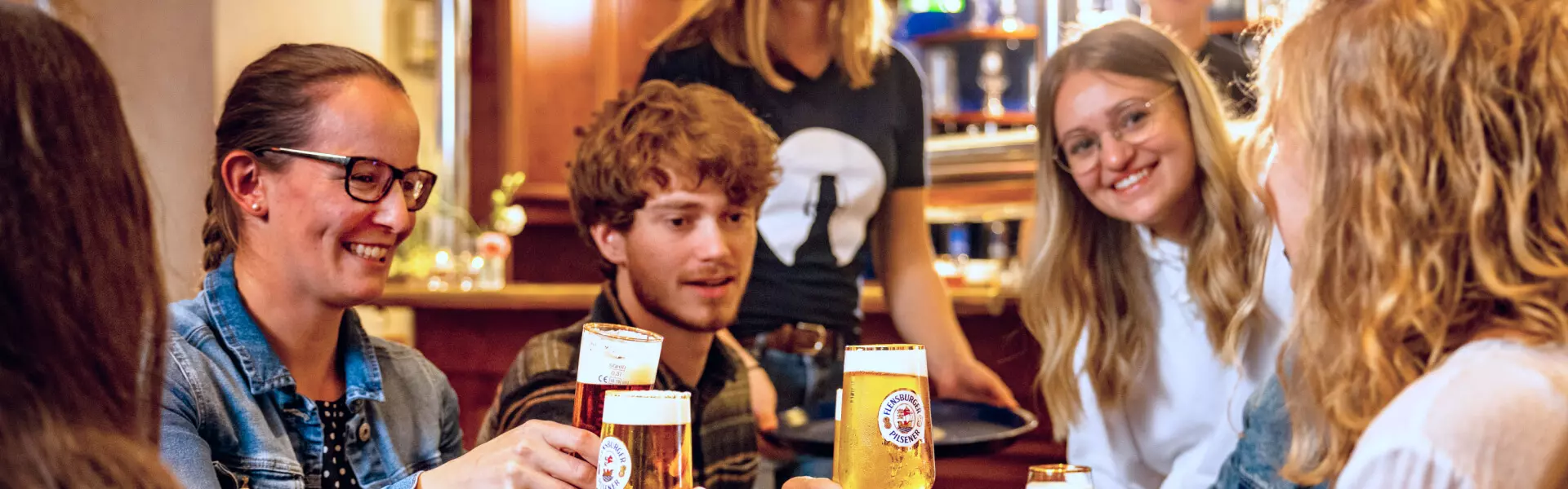 Eine gutgelaunte Gruppe von Menschen stößt mit FLENS vom Fass im Flensburger Salon an.