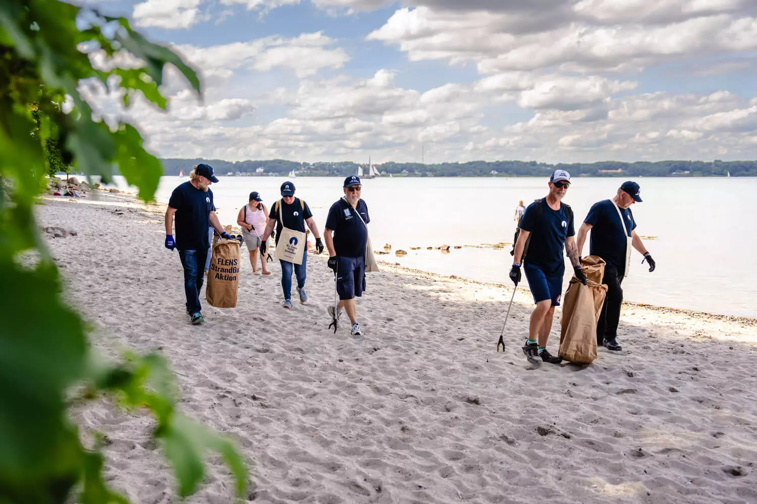 StrandGut-Aktion in Flensburg am Strand, mehrere Leute mit Müllsammeltüten und Müllgreifern.