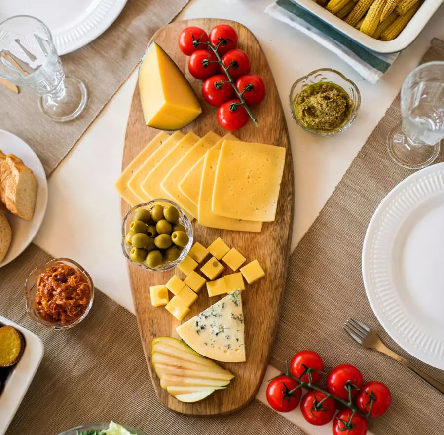 Eine bunte Käseplatte von oben mit verschiedenen Sorten Käse und ein paar Snacktomaten und Oliven.