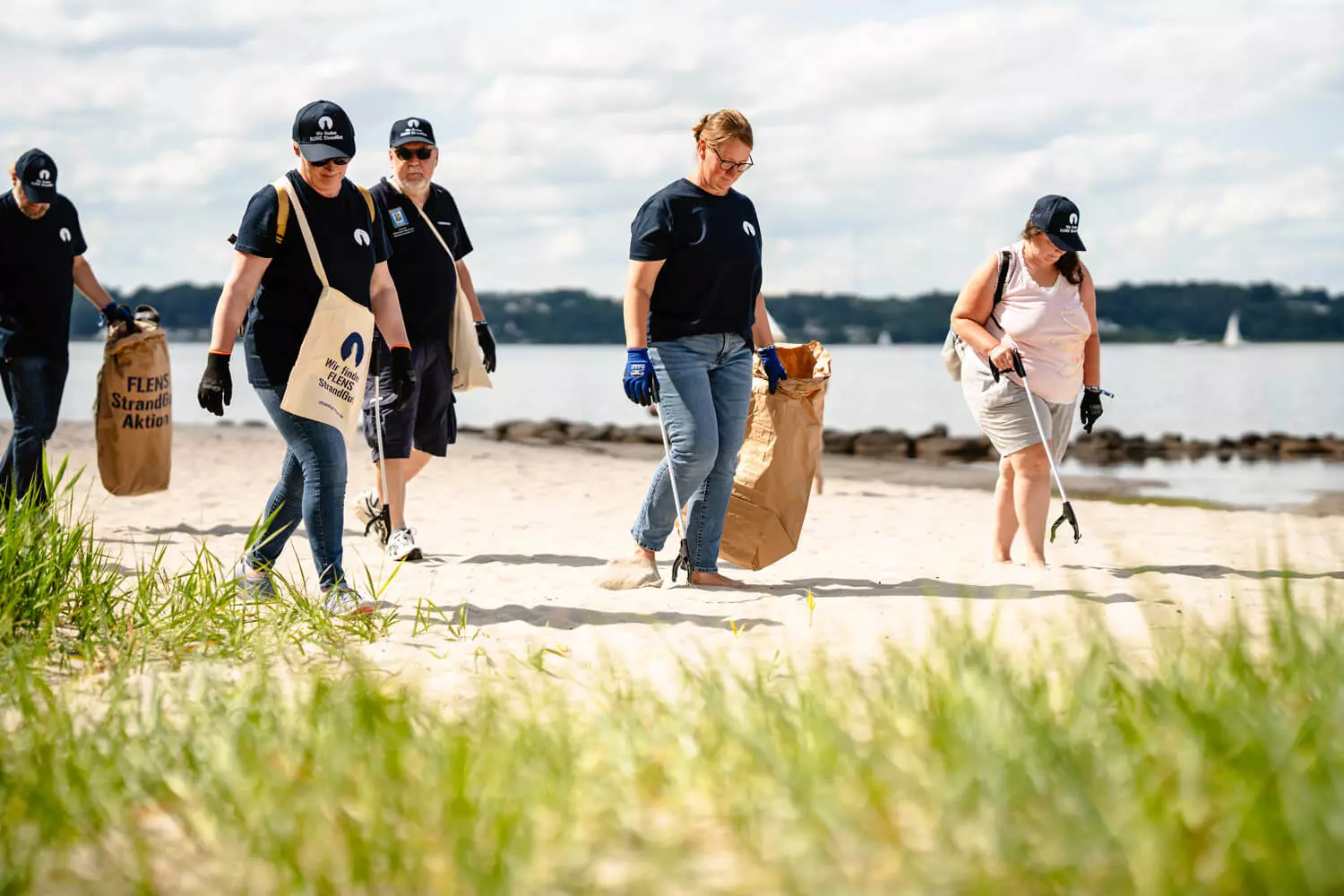 Gruppe von Leuten sammelt Müll am Strand bei einer FLENS StrandGut-Aktion.