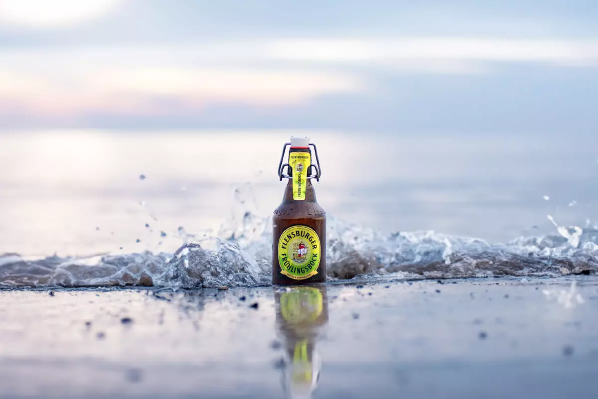 Eine Flasche Flensburger Frühlingsbock steht in der Brandung am Meer in der Welle.