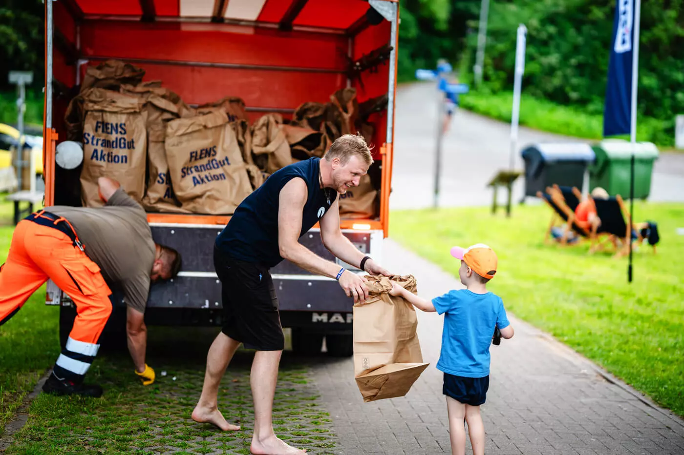 Ein kleiner Junge reicht seine Mülltüte an eine Person, die sie auf den TBZ-Wagen heben will.