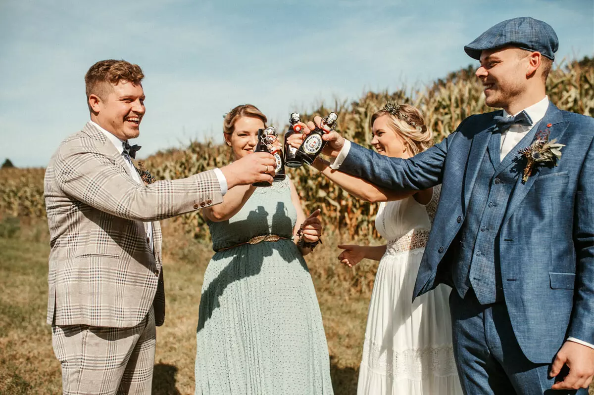 Ein Hochzeitspaar und zwei Gäste stoßen draußen mit Flensburger Gold an.