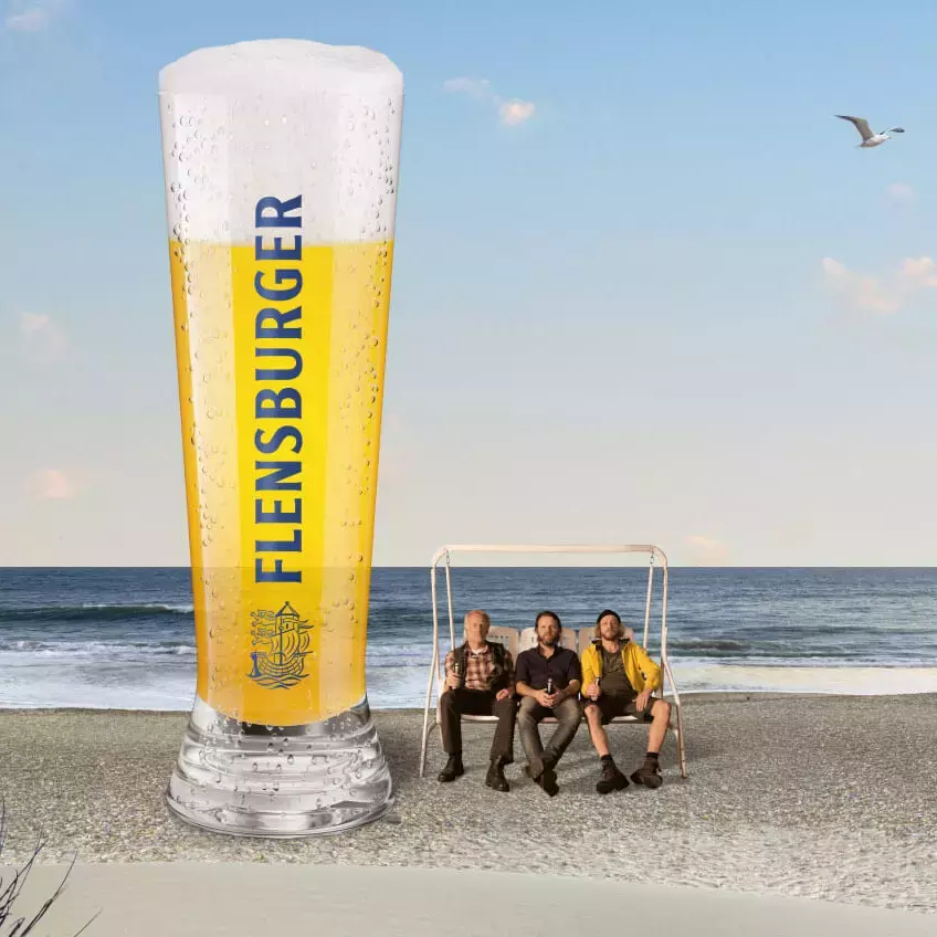 Strandszene mit drei Männer auf einer Hollywood-Schaukel, daneben ein überdimensionales Bierglas.