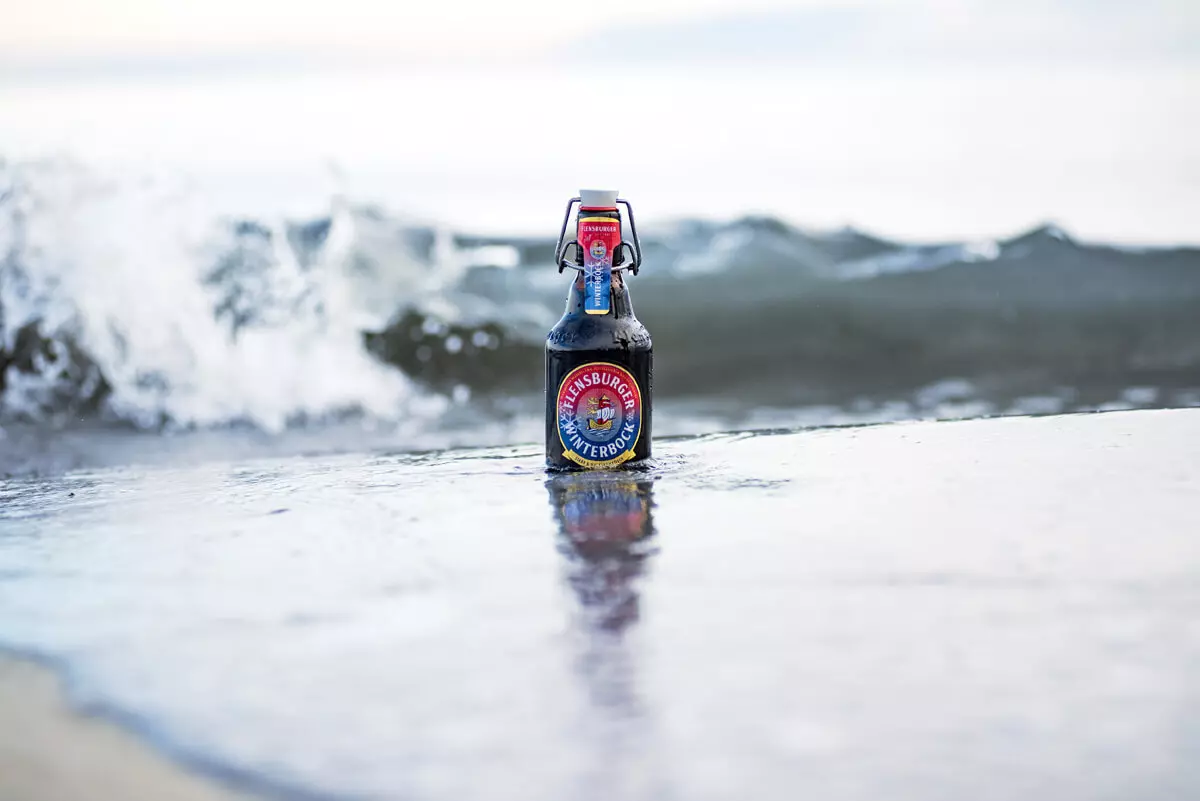 Eine Flasche Flensburger Winterbock steht in der Brandung am Meer in der Welle.