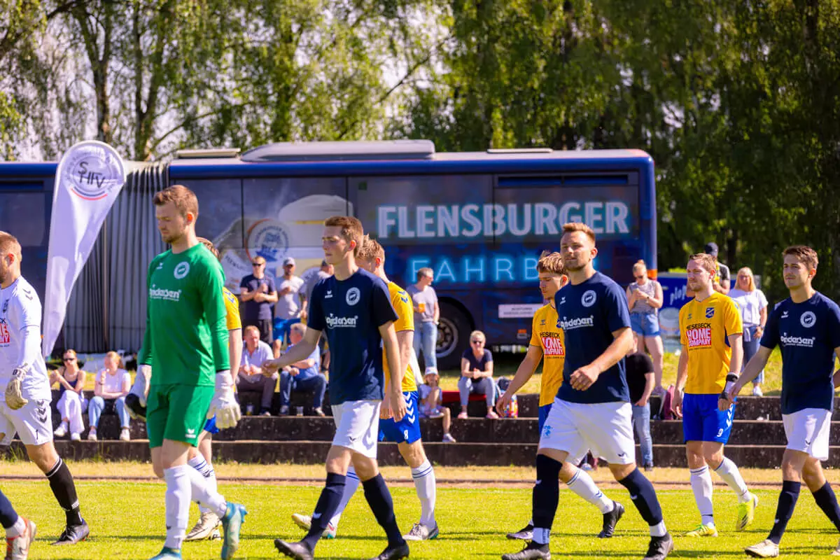 Ein Fußballmannschaft läuft aufs Feld, im Hintergrund die Flensburger Fahrbar.