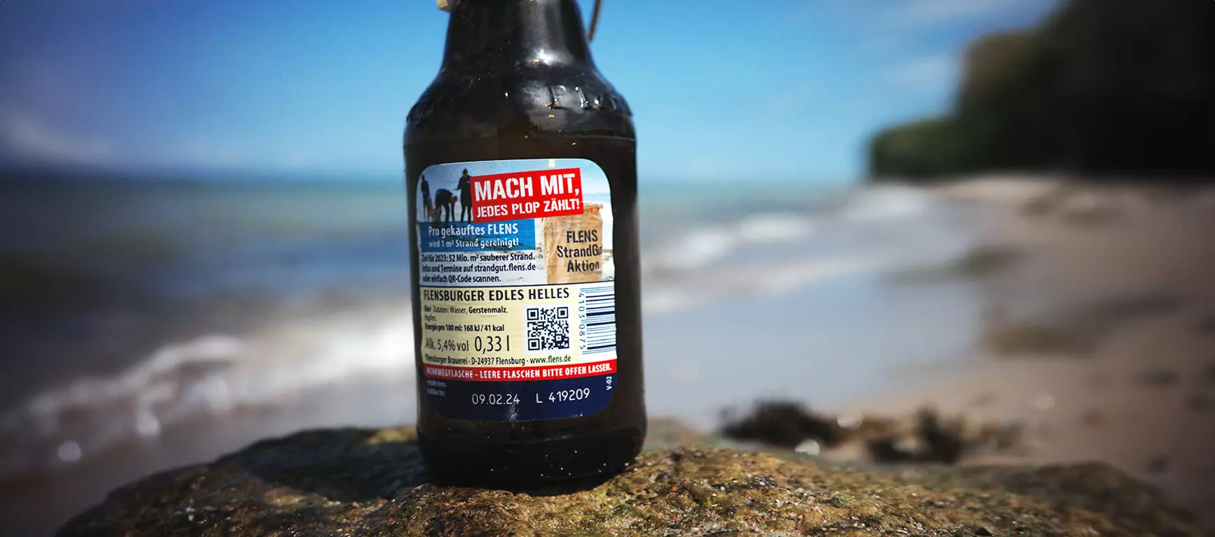 Rückenetikett mit MHD und Losnummer vom Flensburger Edles Helles auf Stein am Strand.