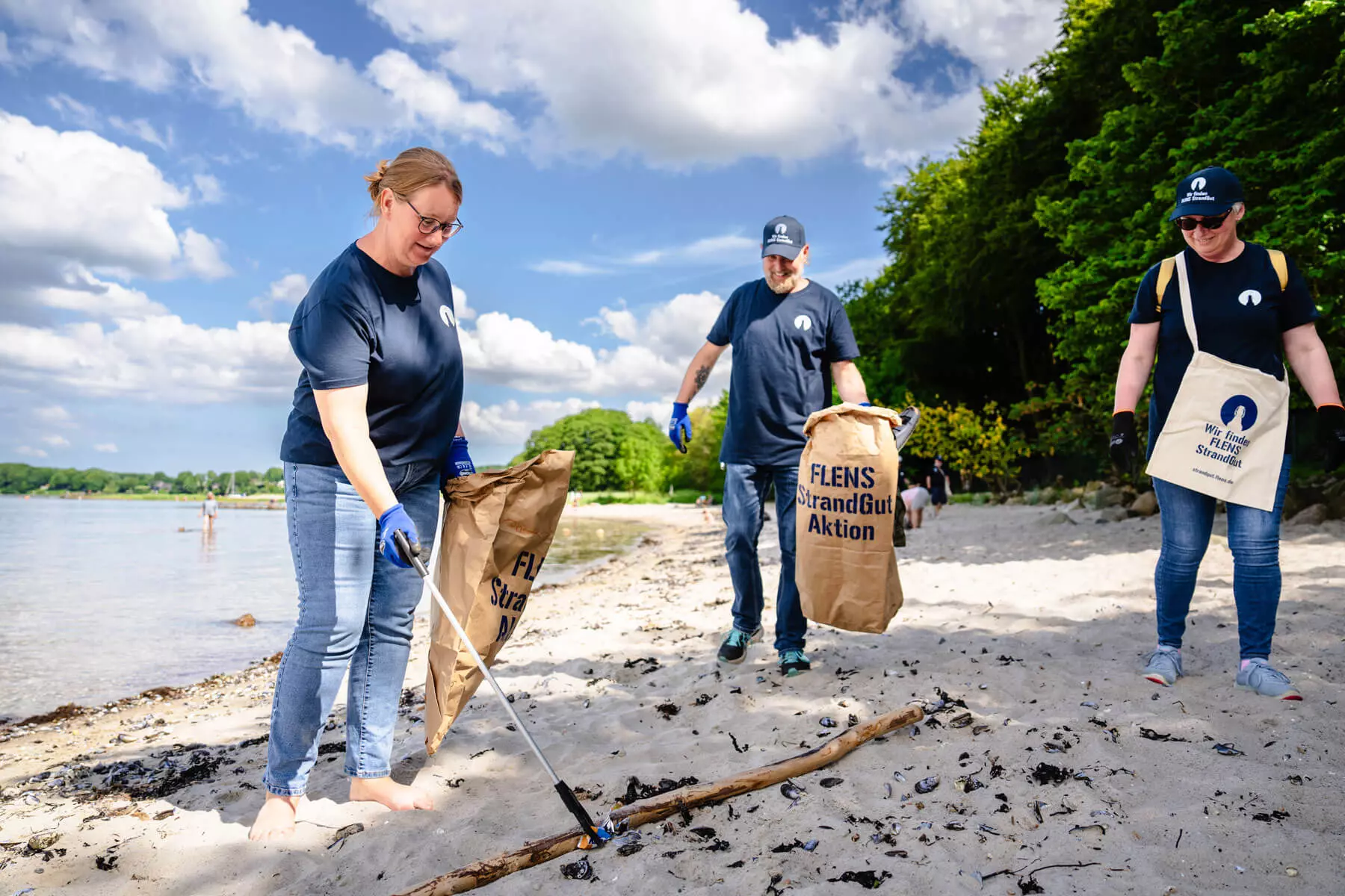 Drei Helfende am Strand mit Mülltüten und -greifern.