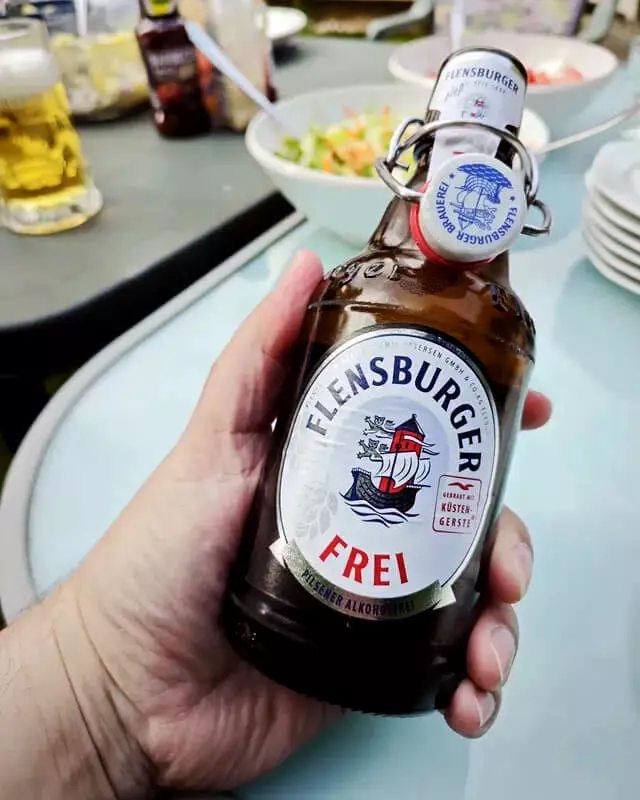 Eine Hand hält eine geöffnete Flasche Flensburger Frei.