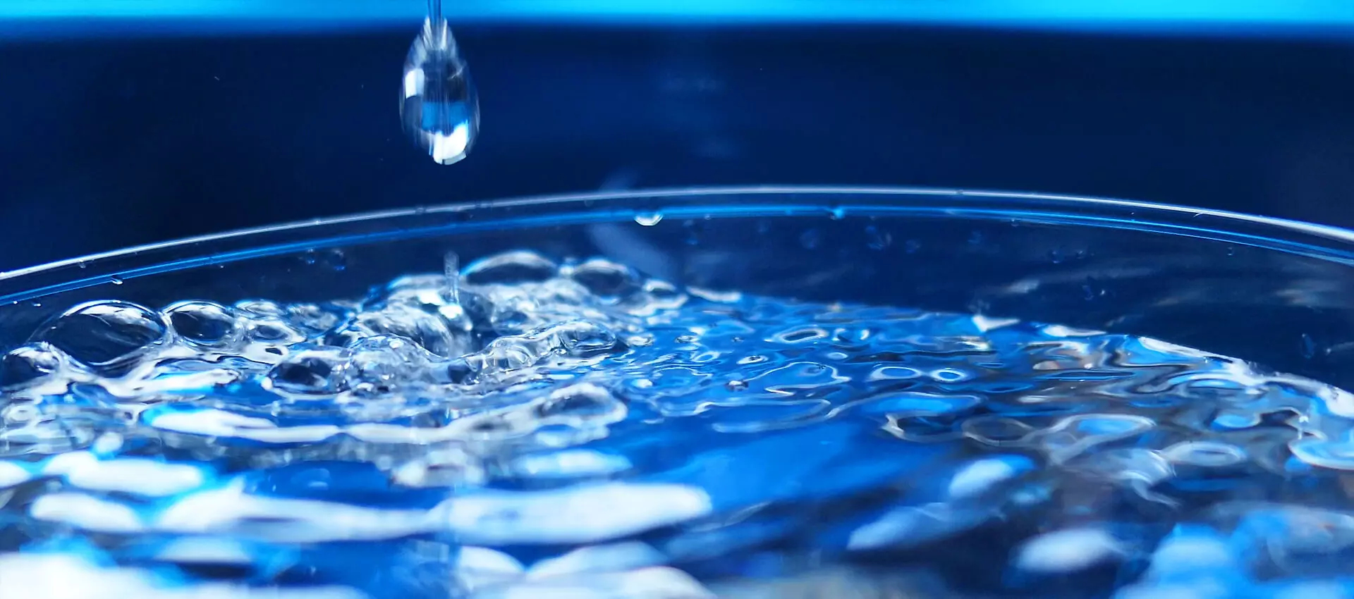 Wasser in einem Glasgefäß, auf die Oberfläche fällt ein Tropfen.