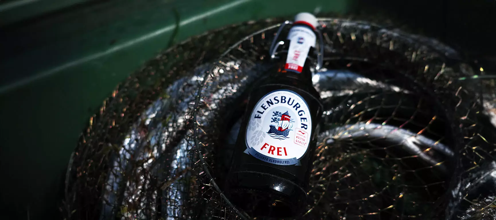 Eine Flasche Flensburger Frei in einem Fischernetz auf einem grünen Boot.