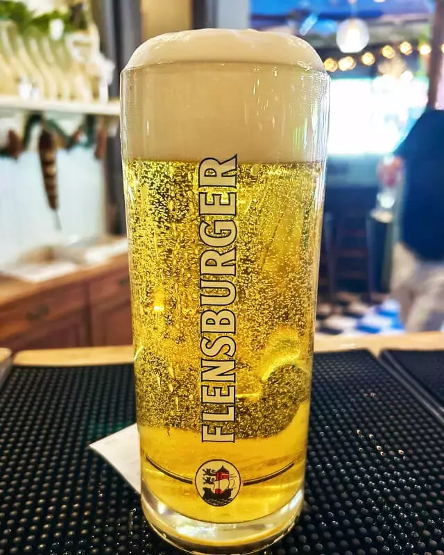 Flensburger Pilsener im Glas mit hoher Schaumkrone und sprudeliger Kohlensäure.